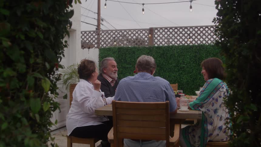 Four older people sitting around a table talking outdoors