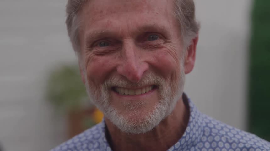 Older man with a gray beard smiles in an outdoor setting
