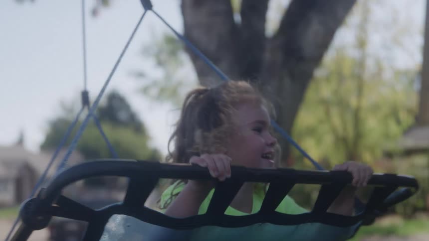 Mother pushes her daughter in a swing hanging from a tree in their front yard on a sunny summer day