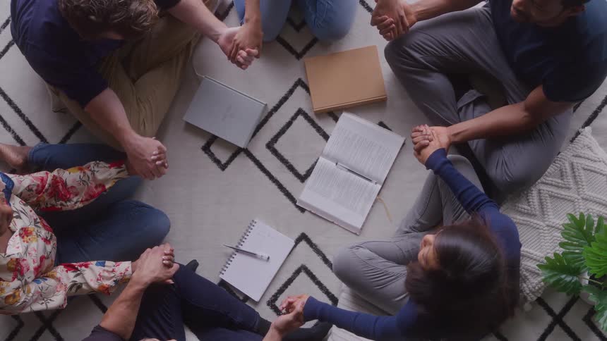 The video is an overhead shot of five people sitting in a circle on a patterned rug actively studying or working on a project they are engaged in a collaborative session with books and notebooks scattered on the floor between them
