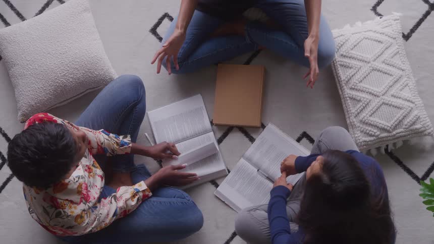 Three people sitting on the floor talk while reading open books