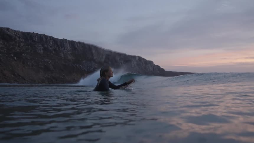 Female surfer on water holding a surf board and moving towards the waves outdoors during dusk or dawn