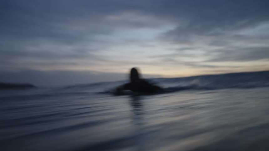 Female surfer turns to catch a swelling wave under a red tinted sky