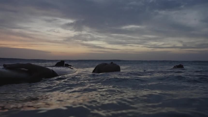 A person rests on a surfboard in ocean water at sunset