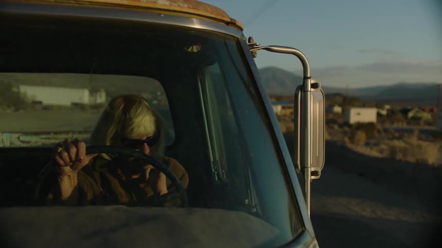 An old blind woman sitting in a pickup is approached by an old man