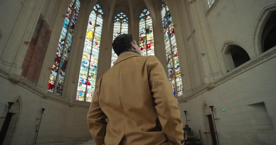 A man in a brown suit stands inside a church gazing up at the ornate artistic ceiling with quiet reverence