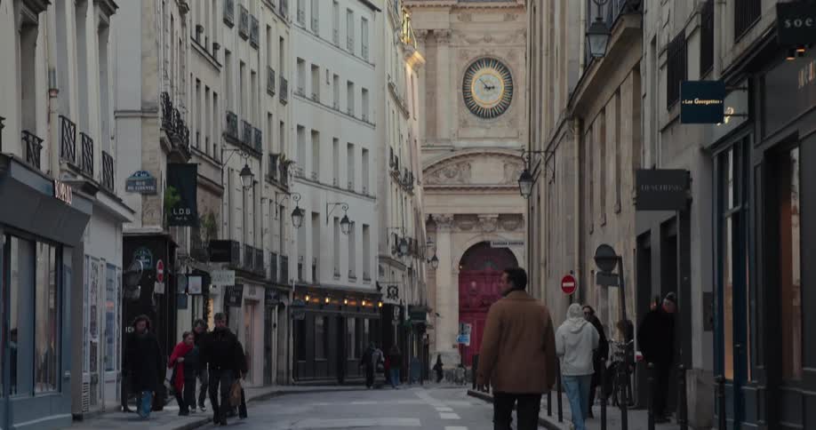 People walk past the shops lining a street leading towards a cathedral on a winter day