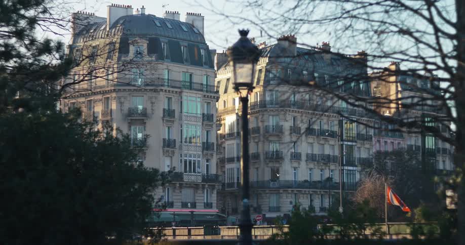 A scenic static shot captures ornate parisian apartment buildings at sunrise framed by a classic lamppost and silhouetted tree branches