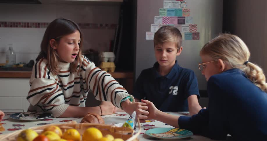 Three children sit around a dining table intently focused on playing a hand game together