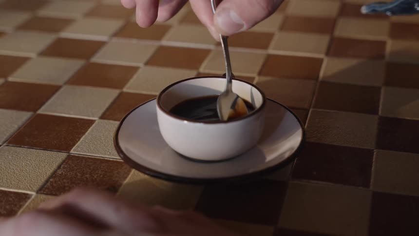 Close up of a person stirring a cup of coffee with a spoon on a table