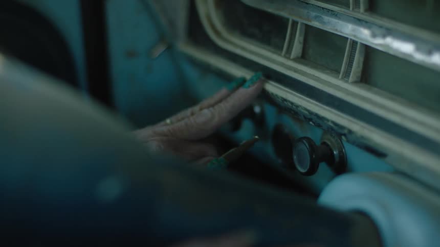 An elderly woman touches the the dashboard of an old pickup truck searching for the ignition