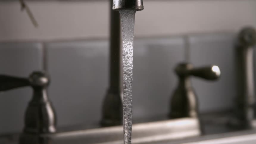 Water flows from kitchen faucet with tiled background and metallic surface