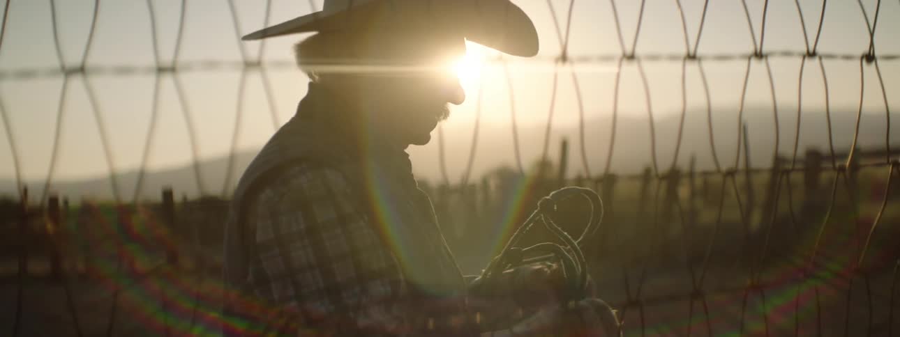 An elderly man wearing a cowboy hat pulls a rope down from a fence
