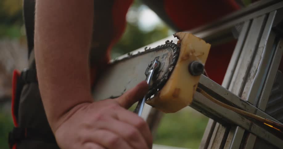 The video is a closeup of a persons hands holding a running chainsaw by the metal guide they appear to be adjusting the chain as it moves over a bright yellow block