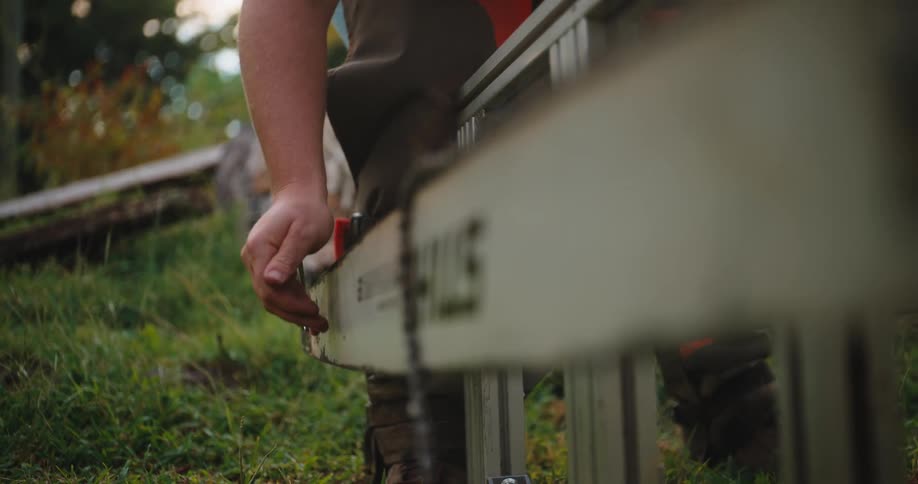 Hand adjusts the mechanism of a chainsaw resting on the grass
