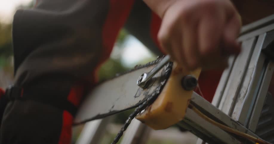 A male tightens a chainsaw chain with a wrench on the guide bar in a closeup