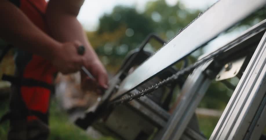 Man adjusts the chain of a saw on a metal stand