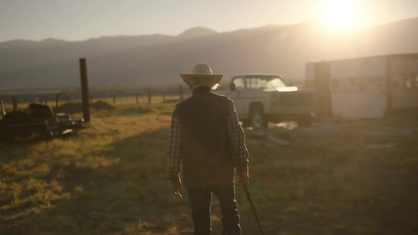 An elderly cowboy walks with a gun in a rural area