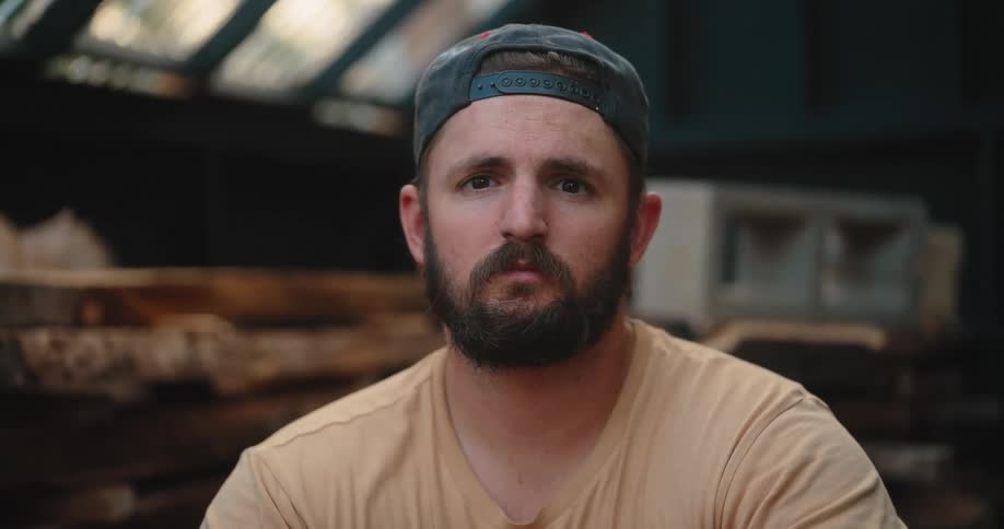 Man with cap on backwards faces in carpentry environment