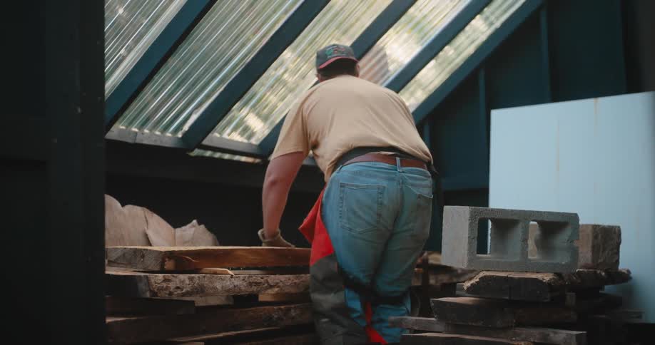 Man stacks large wooden planks inside the shed