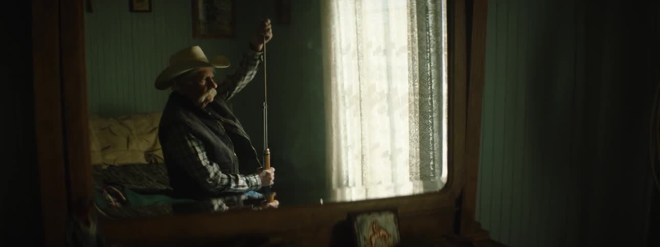 An old man loads his rifle while he sits on his bed