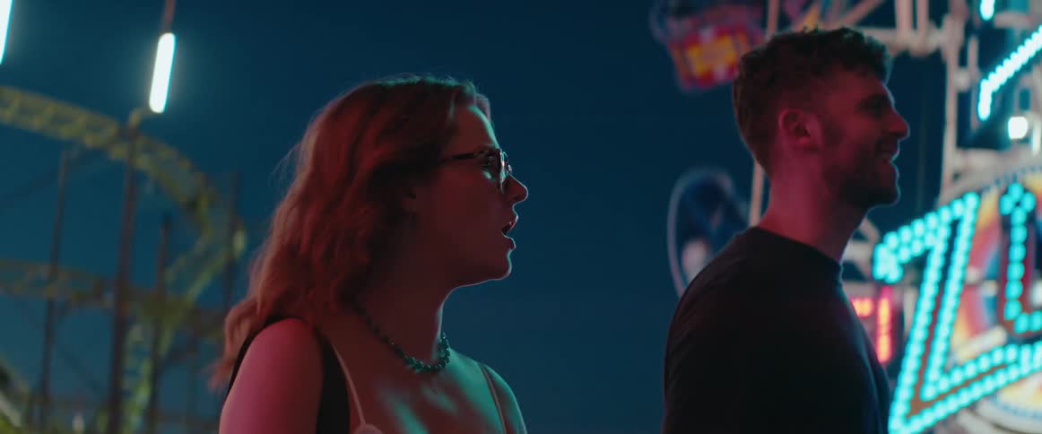 Close up of a young couple conversing while walking together in an amusement park at night