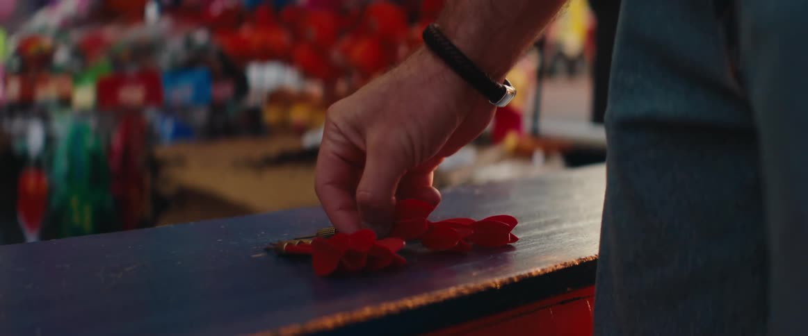 The man picks up a dart from the carnival game
