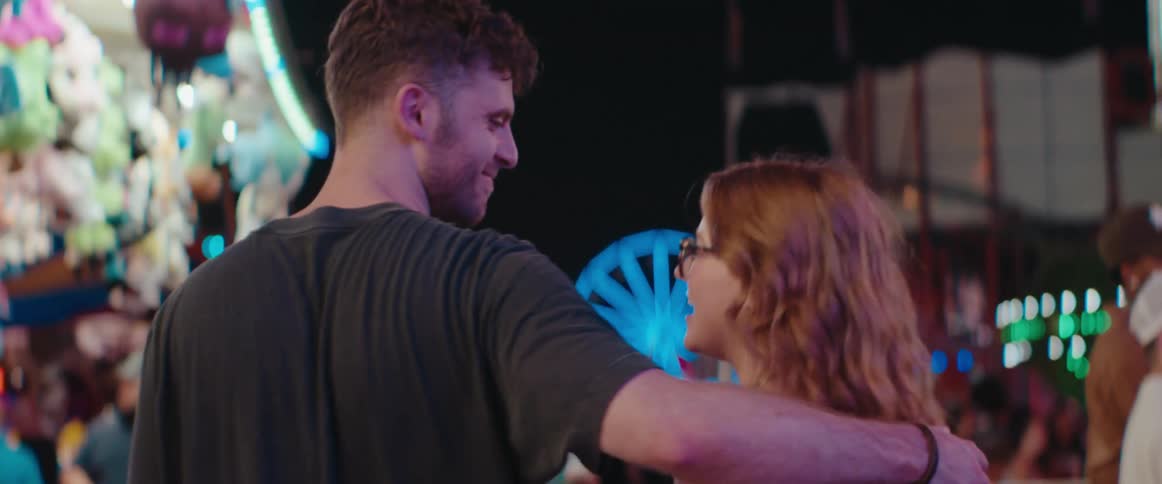 A man and woman laugh and talk while walking through a carnival at night
