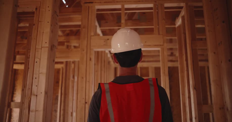 Construction worker wearing a white helmet inspecting a timber framed house indoors during day time