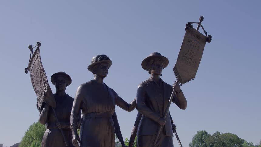 Statue of people carrying banners outdoors with trees on the background during day time