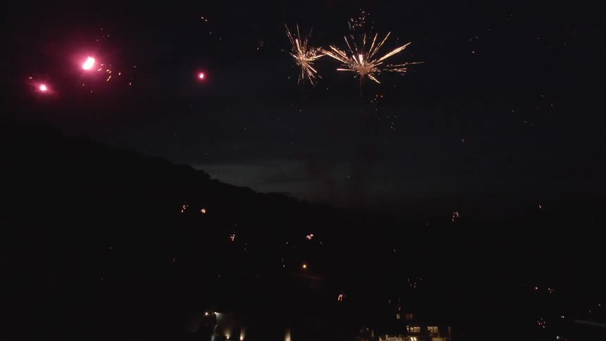 Fireworks explode in the night sky above a brightly lit town