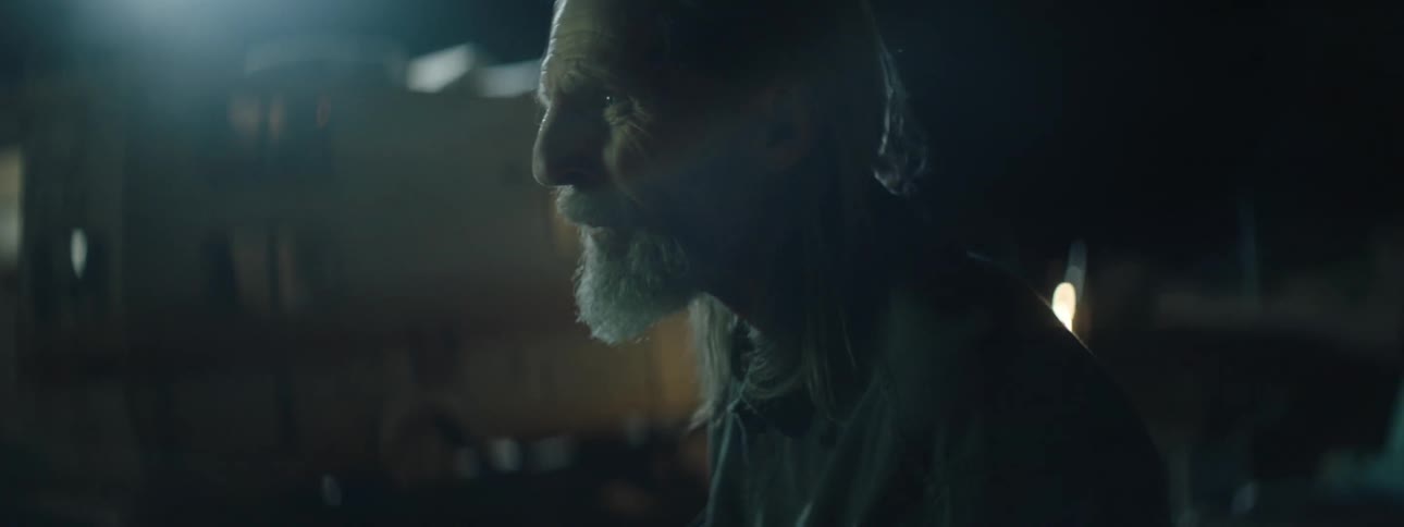 An old man stand outside on a breezy night looking warily around