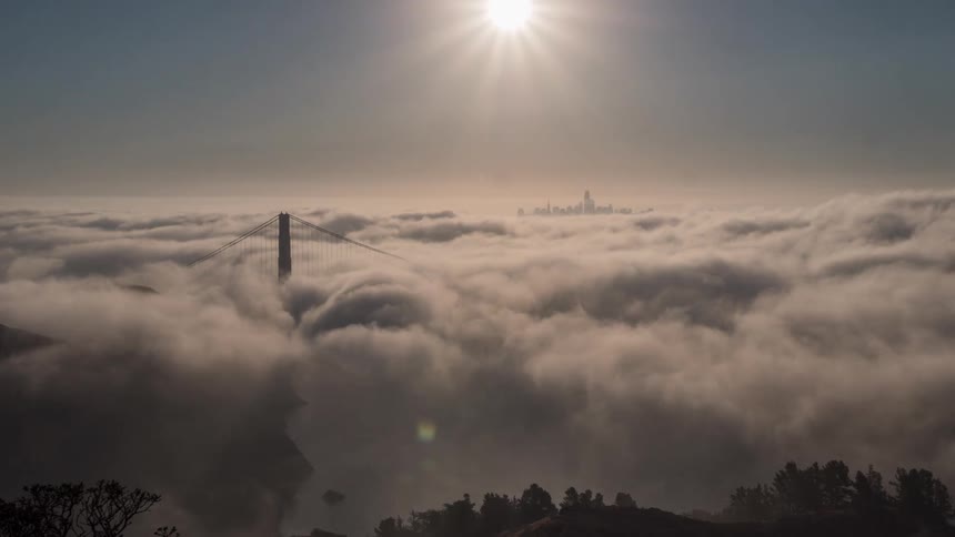Aerial view of golden gate bridge emerging through fog with a distant skyline