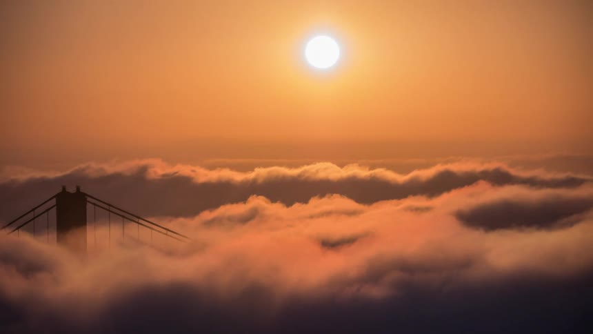 A bridge tower shrouded in clouds under a golden sunset