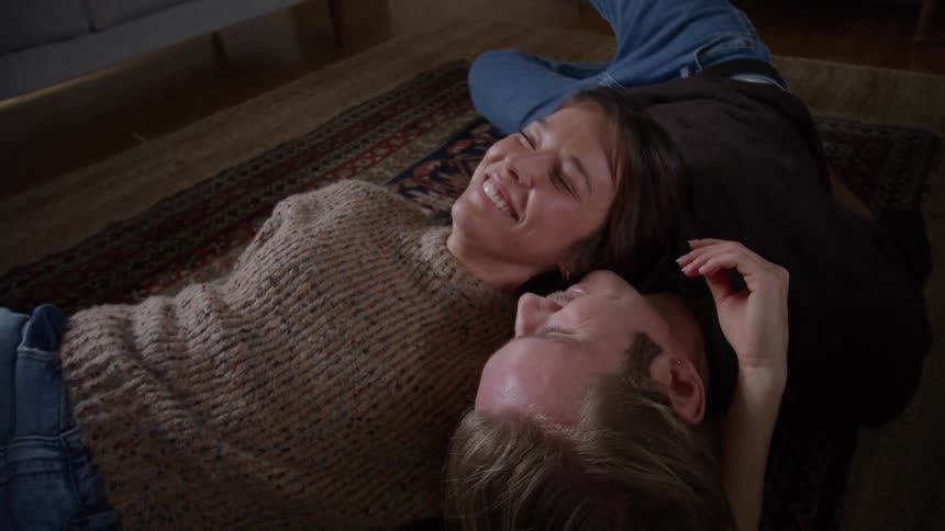 Close up of a young couple conversing while lying together on the floor in a room during daytime