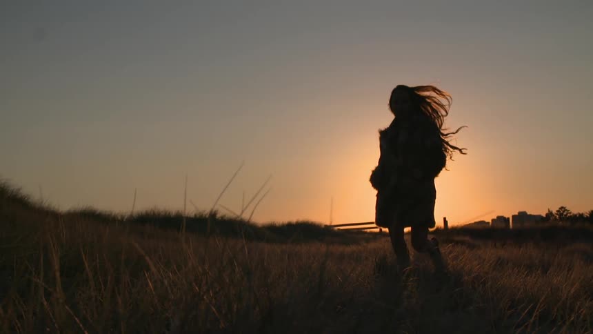 Woman jogging through a field at sunset