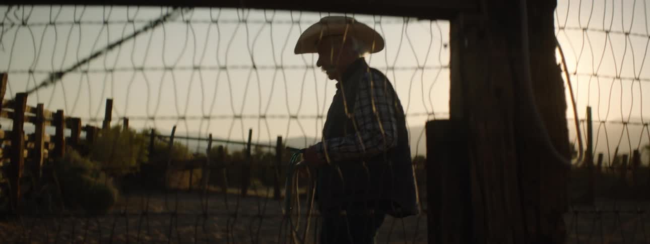 Older man walking outside in fenced enclosure holding a rope
