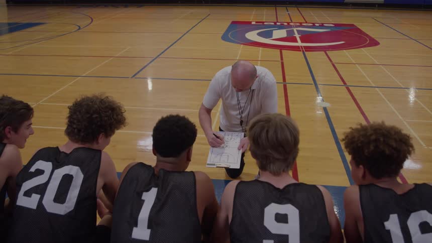 Coach explains a play on the board to the gathered basketball team