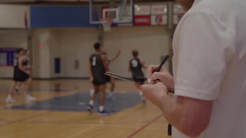 Close of a male coach taking notes at a teen indoor basketball game