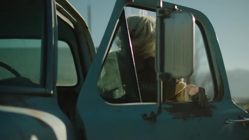 An elderly woman opens the door of an old pickup truck and climbs in