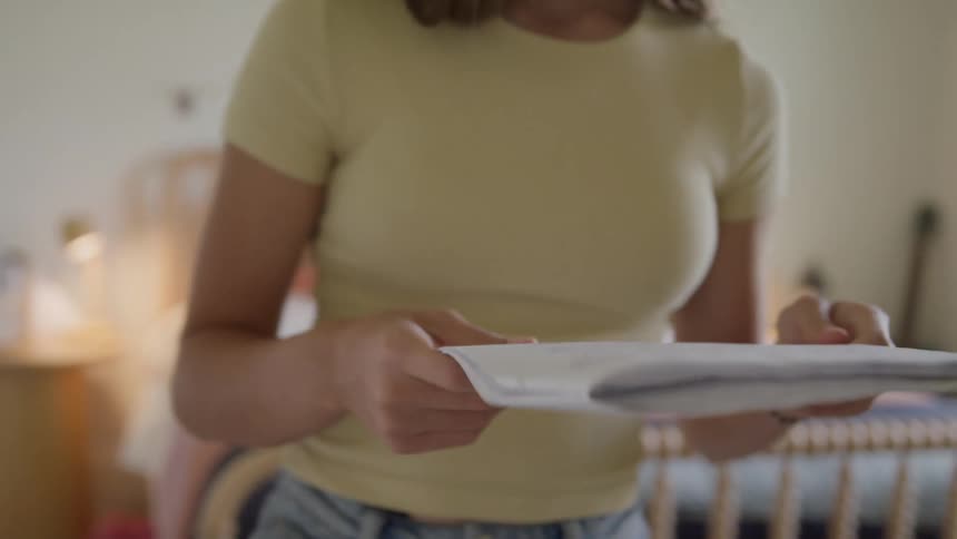 A young female reads from a notebook out loud as she paces in a sunlit bedroom