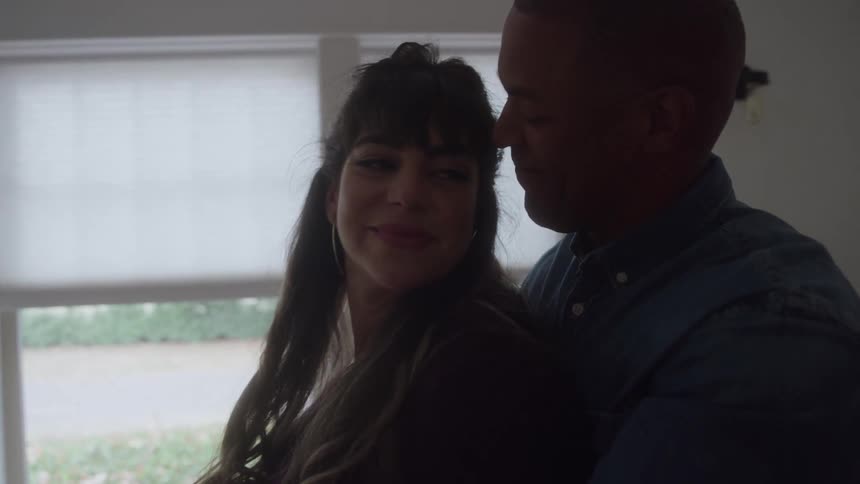 A woman smiles as a man hugs her from behind in a softly lit room