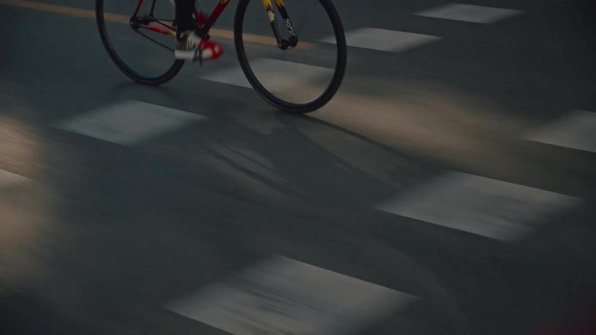 The video shows a cyclist riding a yellow and red fixedgear bicycle down a road in what appears to be the early morning or evening the person is wearing a light blue hoodie and dark pants and the shot focuses on the lower body and the motion of