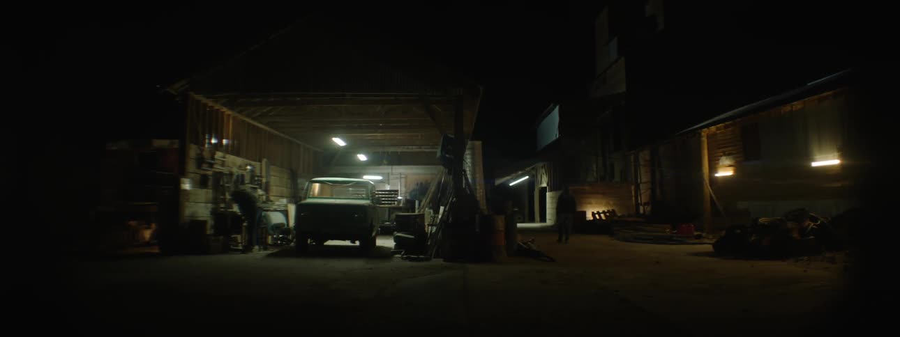 Man welding in open garage at night while another man walks outside