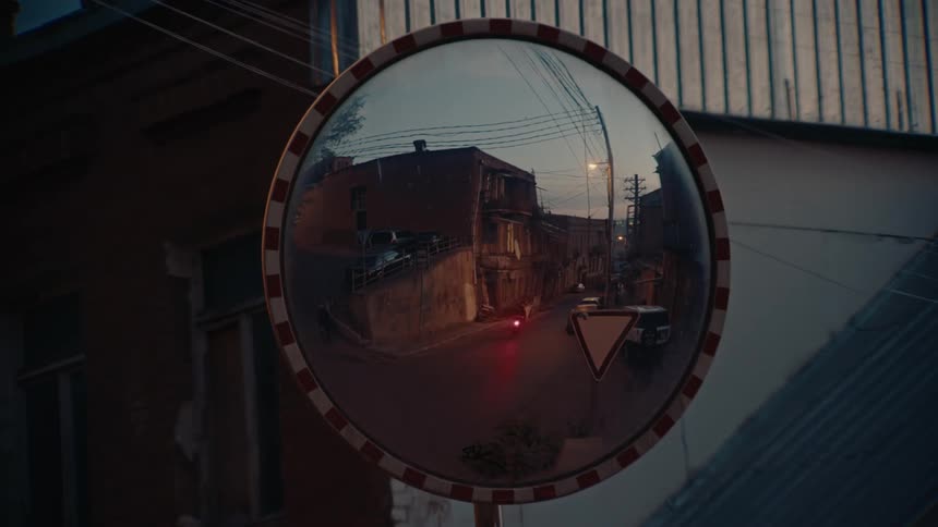 The video is a stationary shot showing a reflection in a large circular convex mirror mounted outdoors the reflection captures a dimly lit narrow street surrounded by old brick buildings suggesting an urban or older town environment
