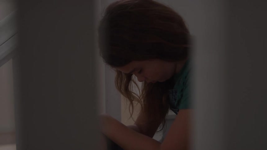 Girl sitting rests her head on her knees in a softly lit corner