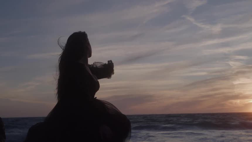 The woman reaches out towards the water on the beach