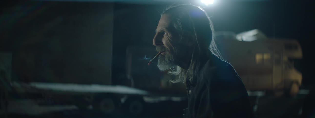 A man with a cigarette in his mouth looks around outside