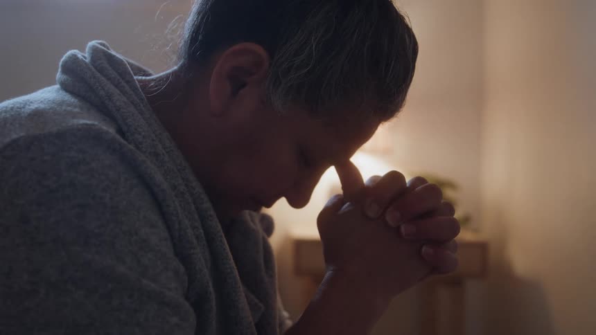 The video is a closeup shot of a womans face in profile with her head bowed and her eyes closed she appears to be praying or deep in thought with her hands clasped near her forehead