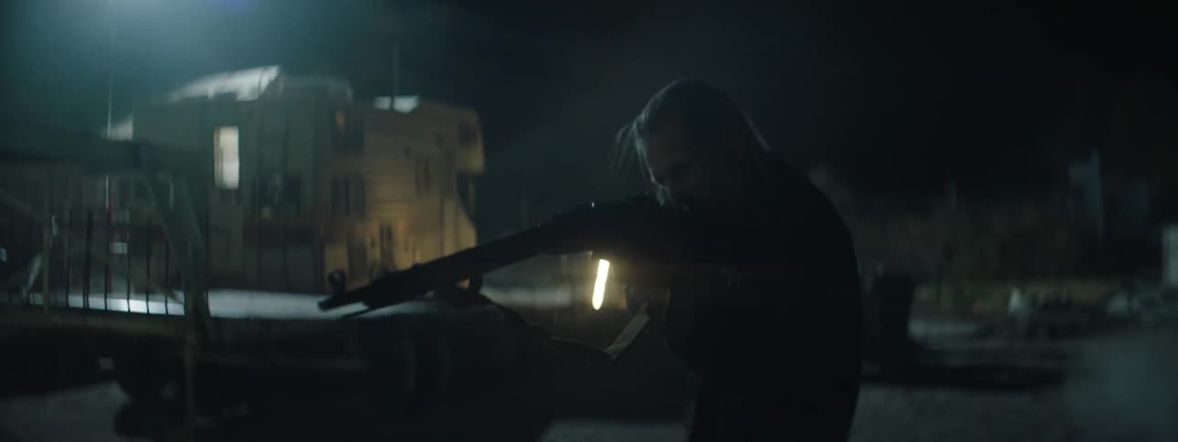 A man aiming a rifle looks around outside